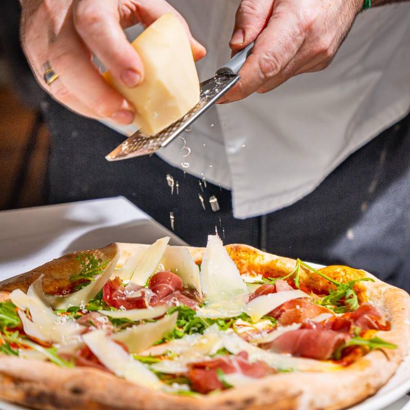 Parmesan grated over a pizza at the table